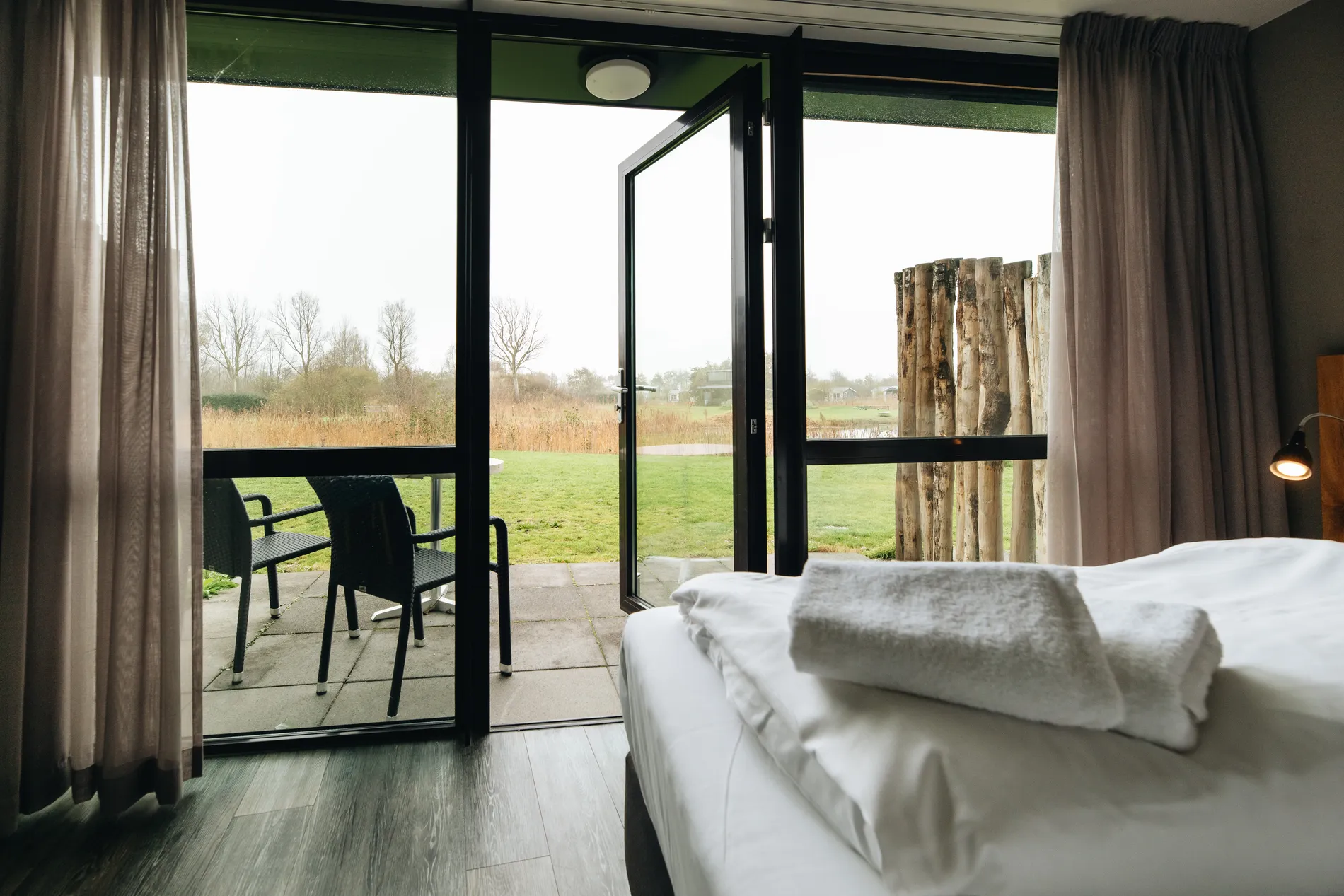 Uitzicht vanuit een hotelkamer op het privéterras en het omliggende Zeeuwse polderlandschap via openslaande deuren.